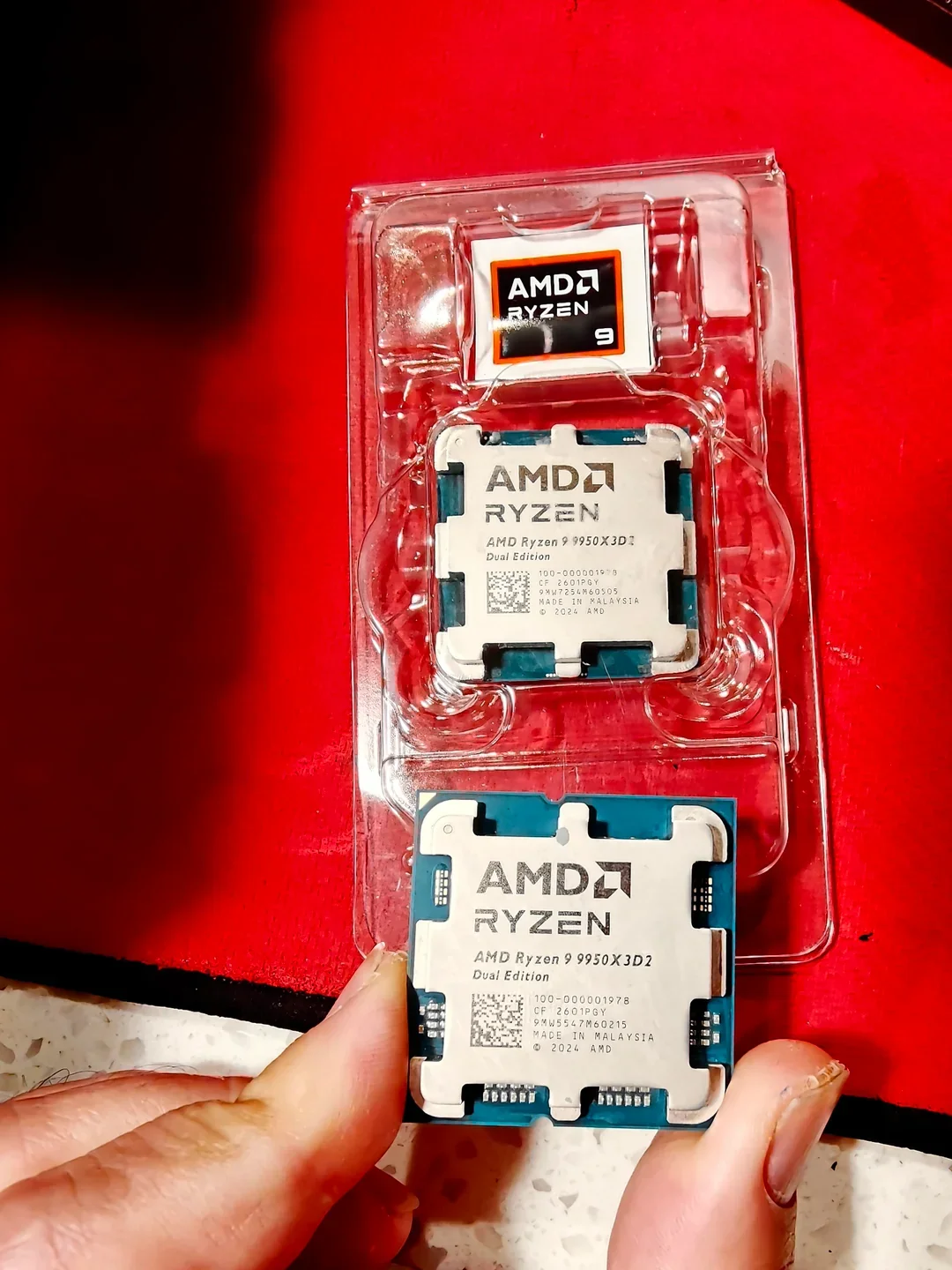 A close-up image of two AMD Ryzen 9 9950X3D2 processors labeled Dual Edition against a red background, with visible AMD branding.