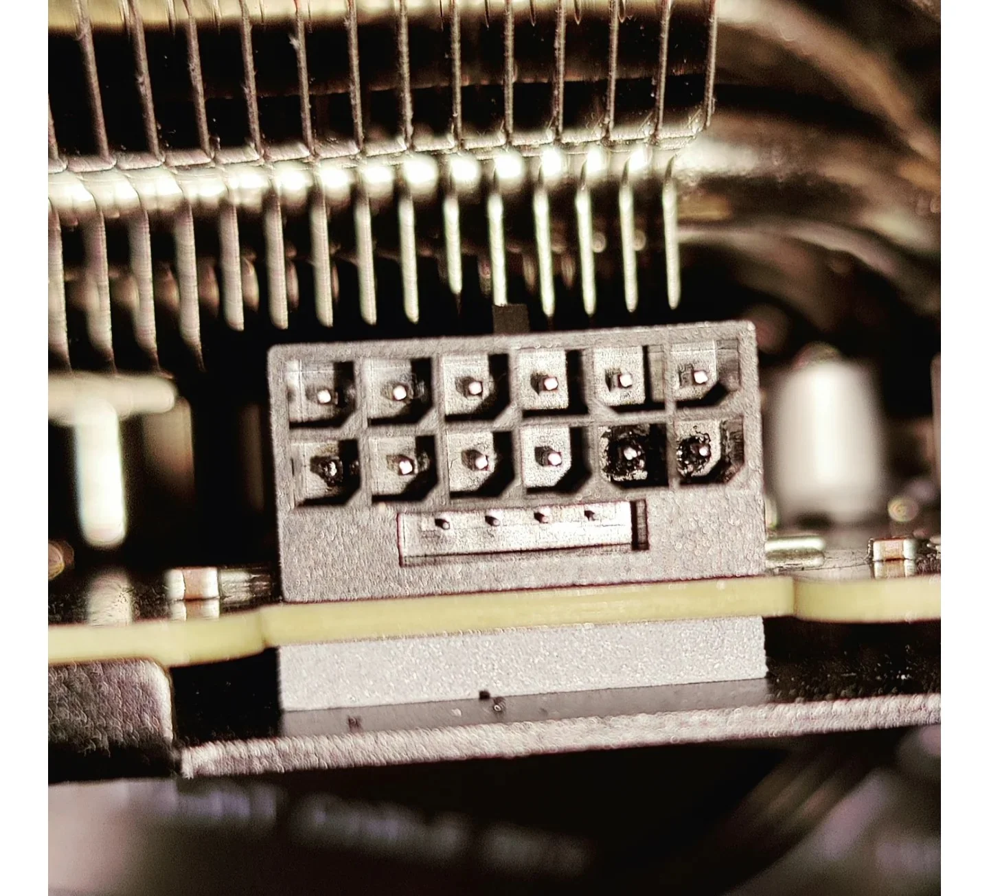 A close-up of a 12-pin GPU power connector with visible burn marks on one pin.
